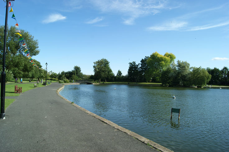 A lake with a row of lampposts next to it, and some people walking past.